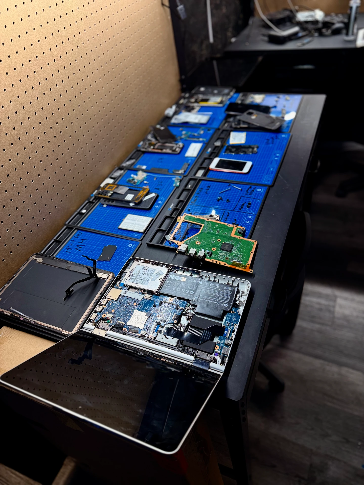 OneClick Phone Repairs technician workbench with devices being repaired in Fullerton, CA